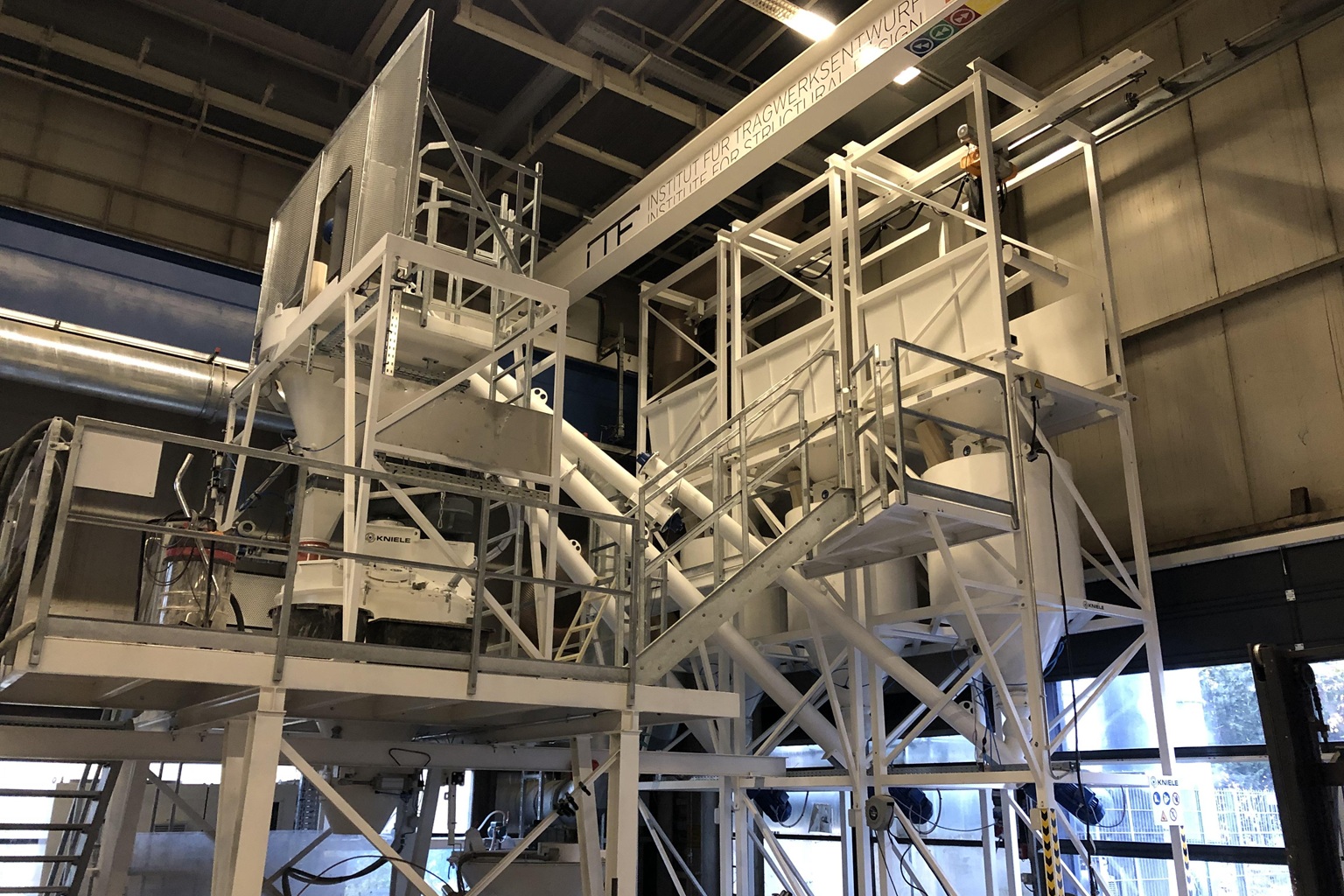 Große Misch- und Förderanlage aus Metall mit Treppen und Plattformen in Industriehalle, technische Versuchsanlage sichtbar.