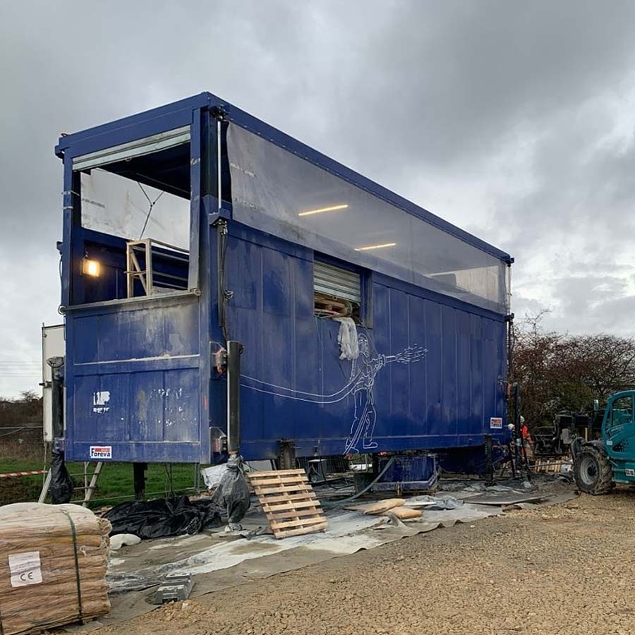 A mobile mixing plant in a blue container on a building site under a cloudy sky.