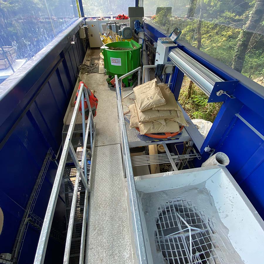 A view inside a mobile mixing plant with a storage hopper, bags of materials and conveyor systems for concrete work.