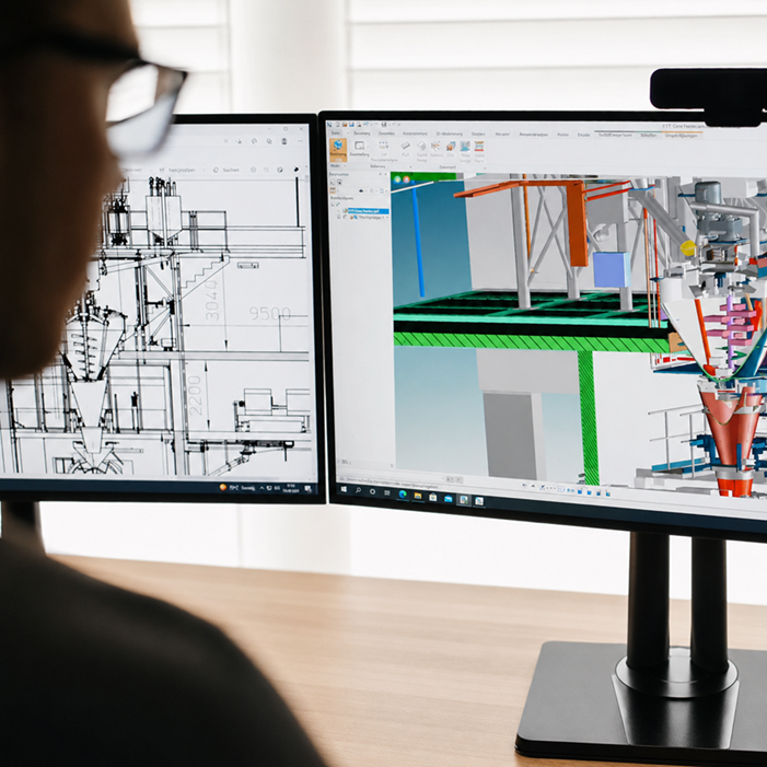 Person arbeitet an zwei Monitoren mit technischer CAD-Zeichnung und 3D-Modell einer Industrieanlage.