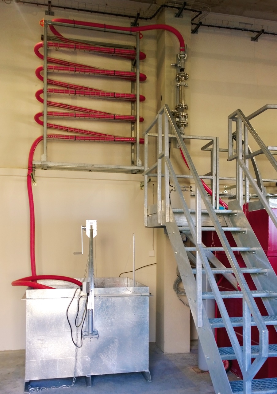 Galvanized square container on the floor in which a red hose protrudes, which is attached to the wall in a zigzag.